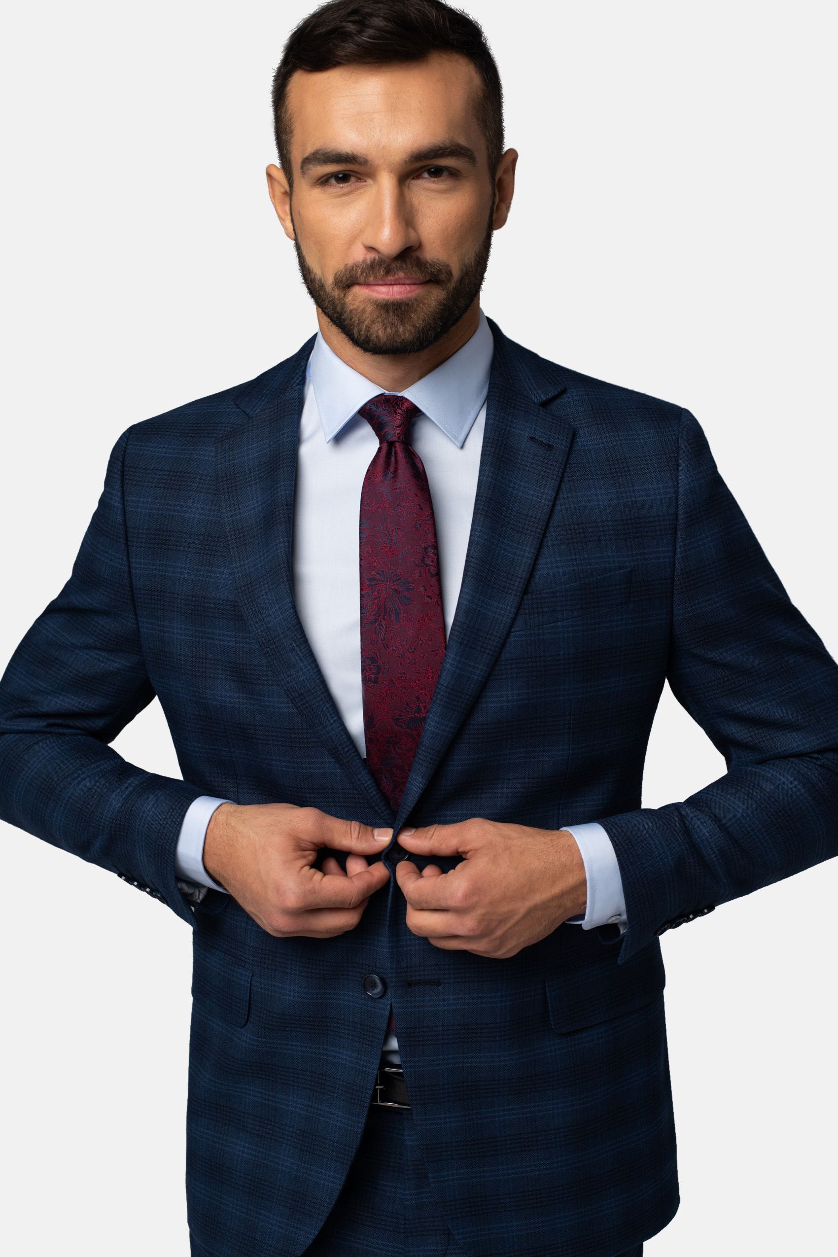 Mężczyzna ubrany w marynarkę granatową w krate, niebieską koszulę, i czerwony krawat