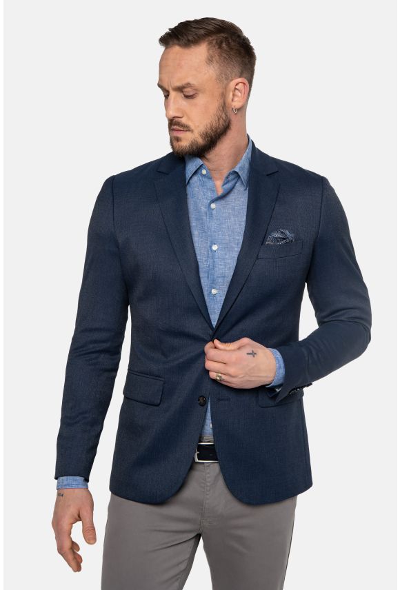 Mężczyzna ubrany w granatową marynarkę, niebieska koszulę i szare spodnie