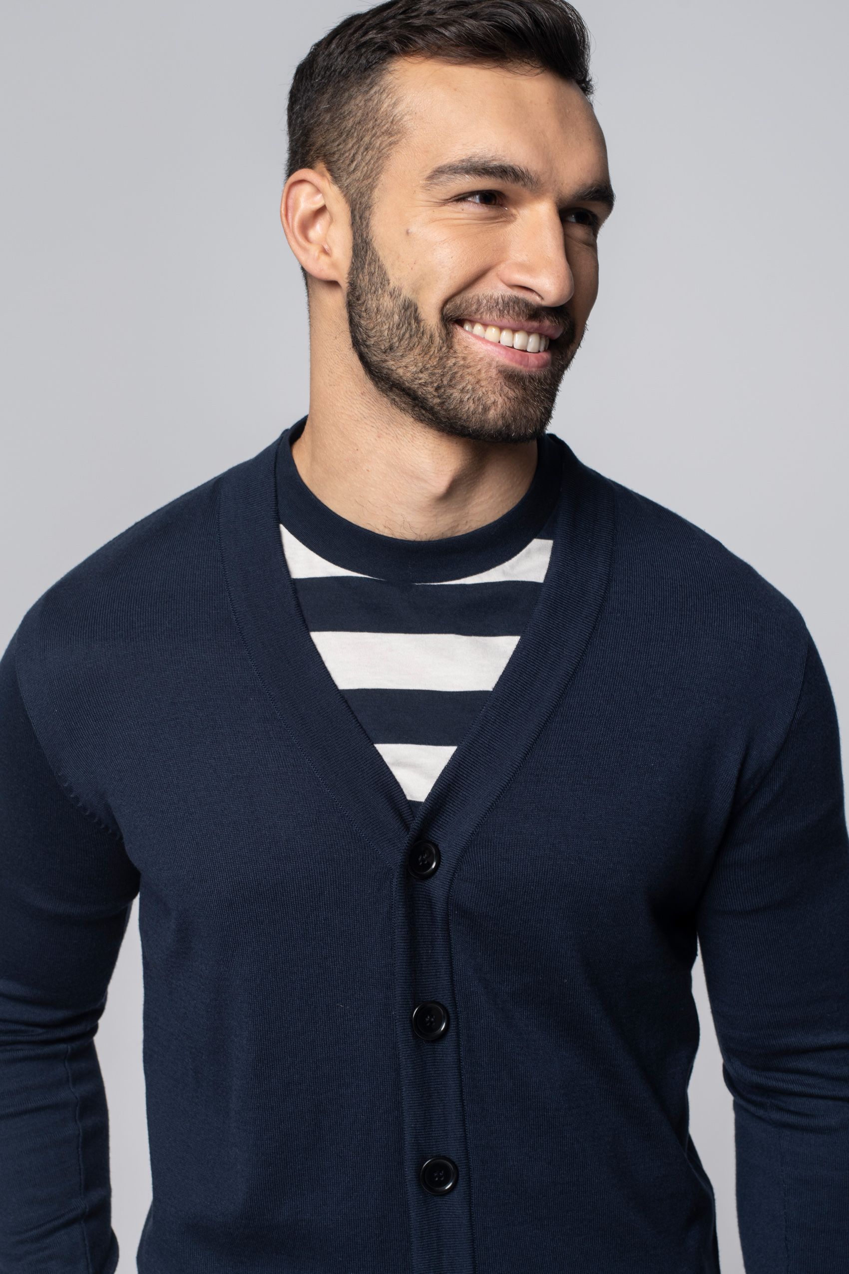 Mężczyzna ubrany w koszulkę w biało-niebieskie paski i granatowy kardigan.