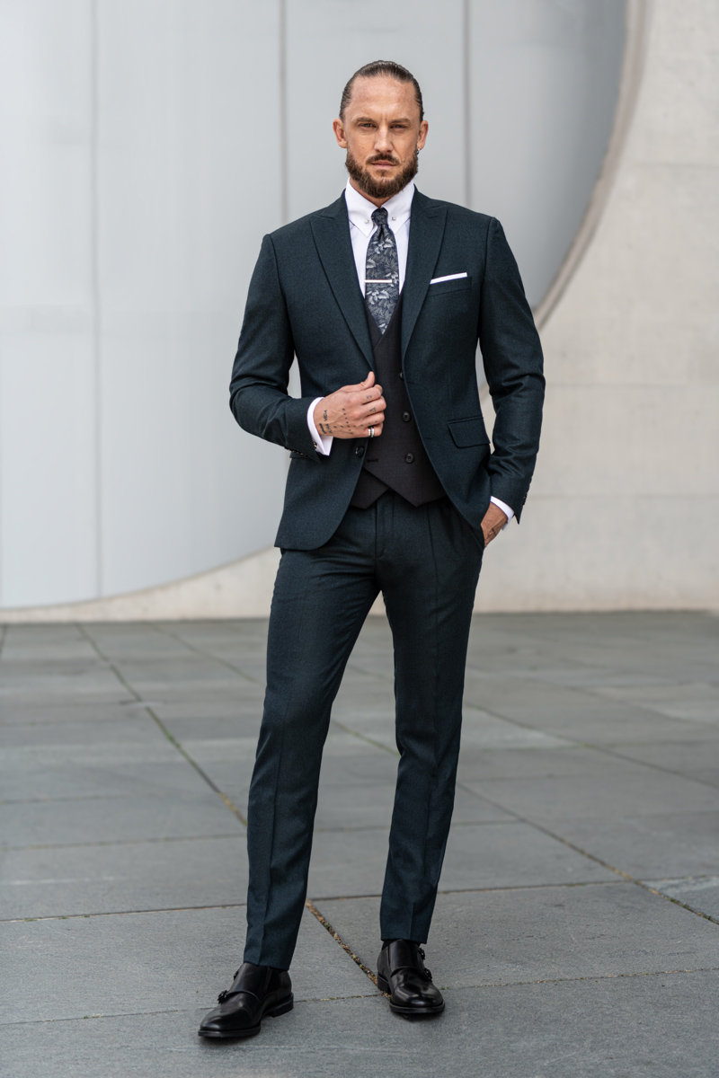 Mężczyzna w ciemnogranatowym garniturze, białej koszuli i czarnej kamizelce z kolorowym krawatem