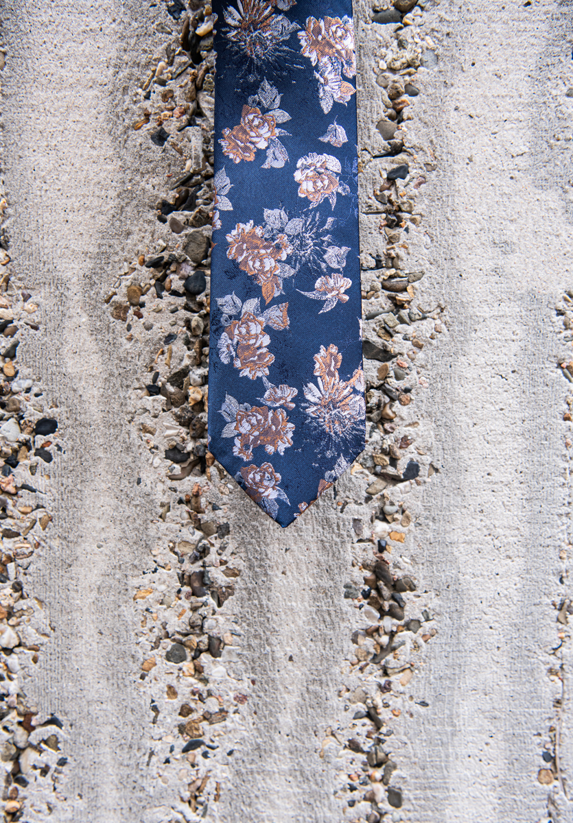 Niebieski krawat z beżowymi kwiatami.