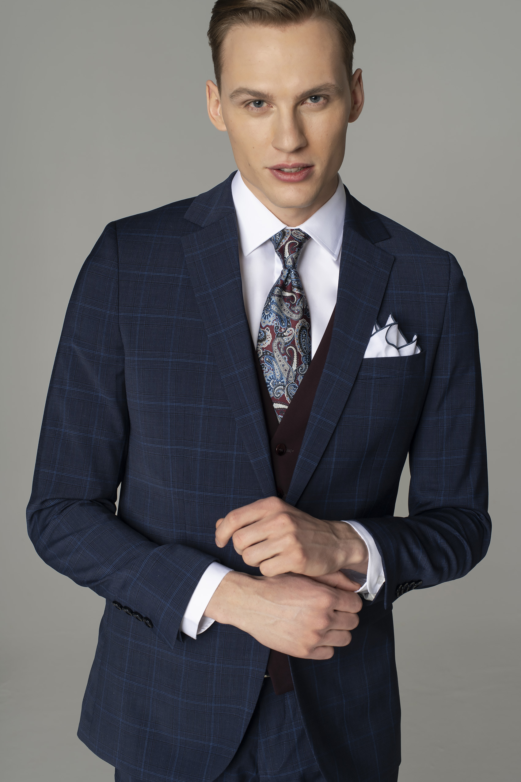 Mężczyzna ubrany w niebieski garnitur w lekką kratę, białą koszulę i krawat