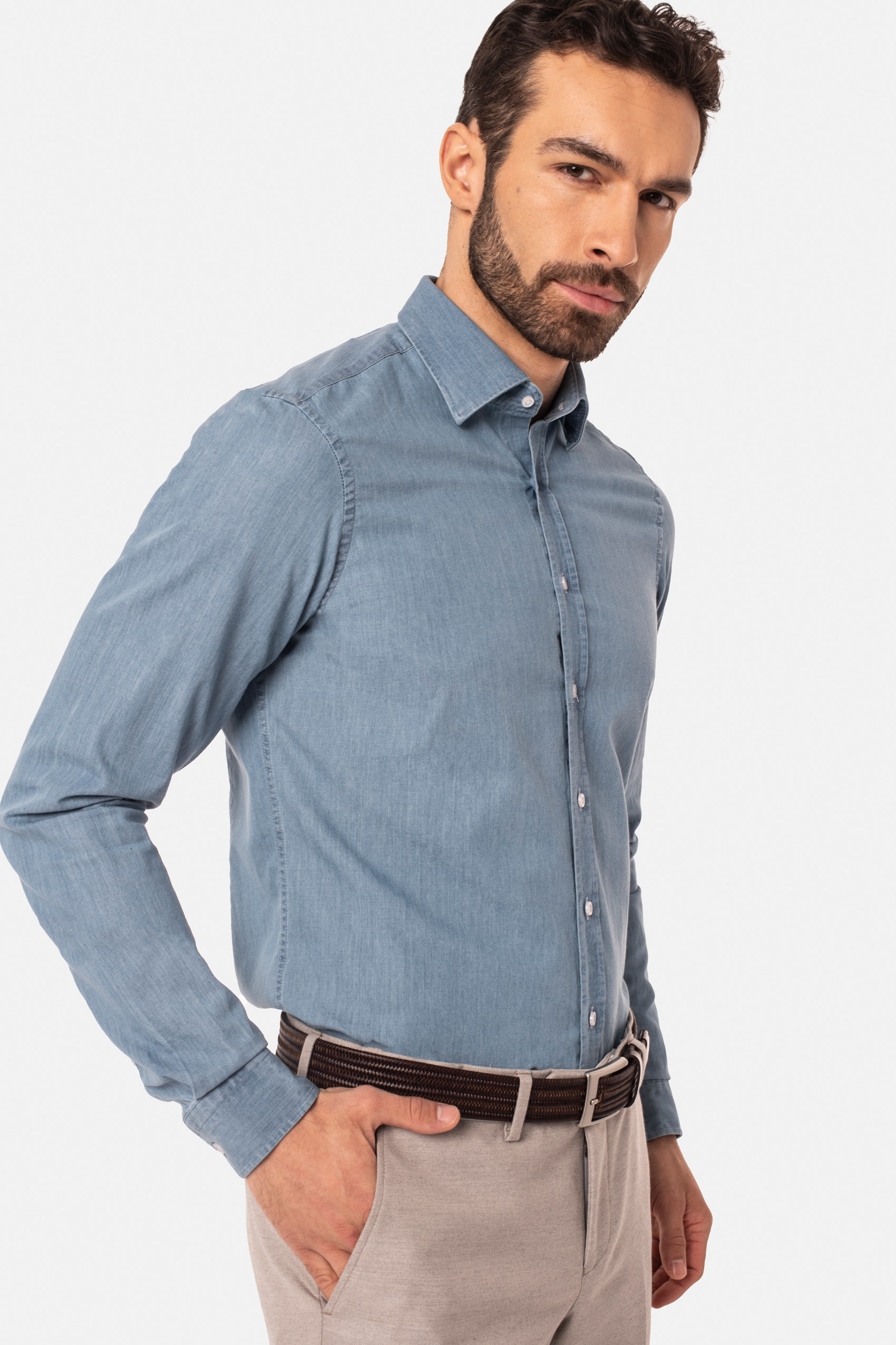 Model ubrany w jasnoniebieską koszulę z guzikami, jasne beżowe spodnie z brązowym paskiem