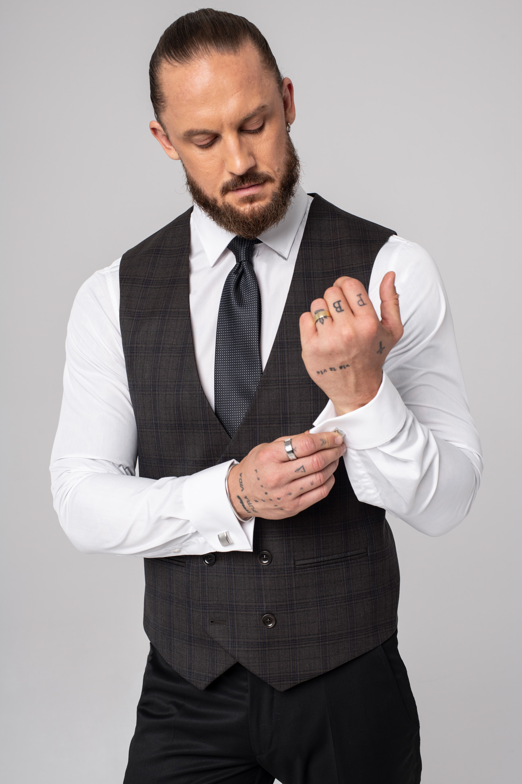 Mężczyzna ubrany w białą koszulę, kamizelkę brązową w kratę, krawat i czarne spodnie