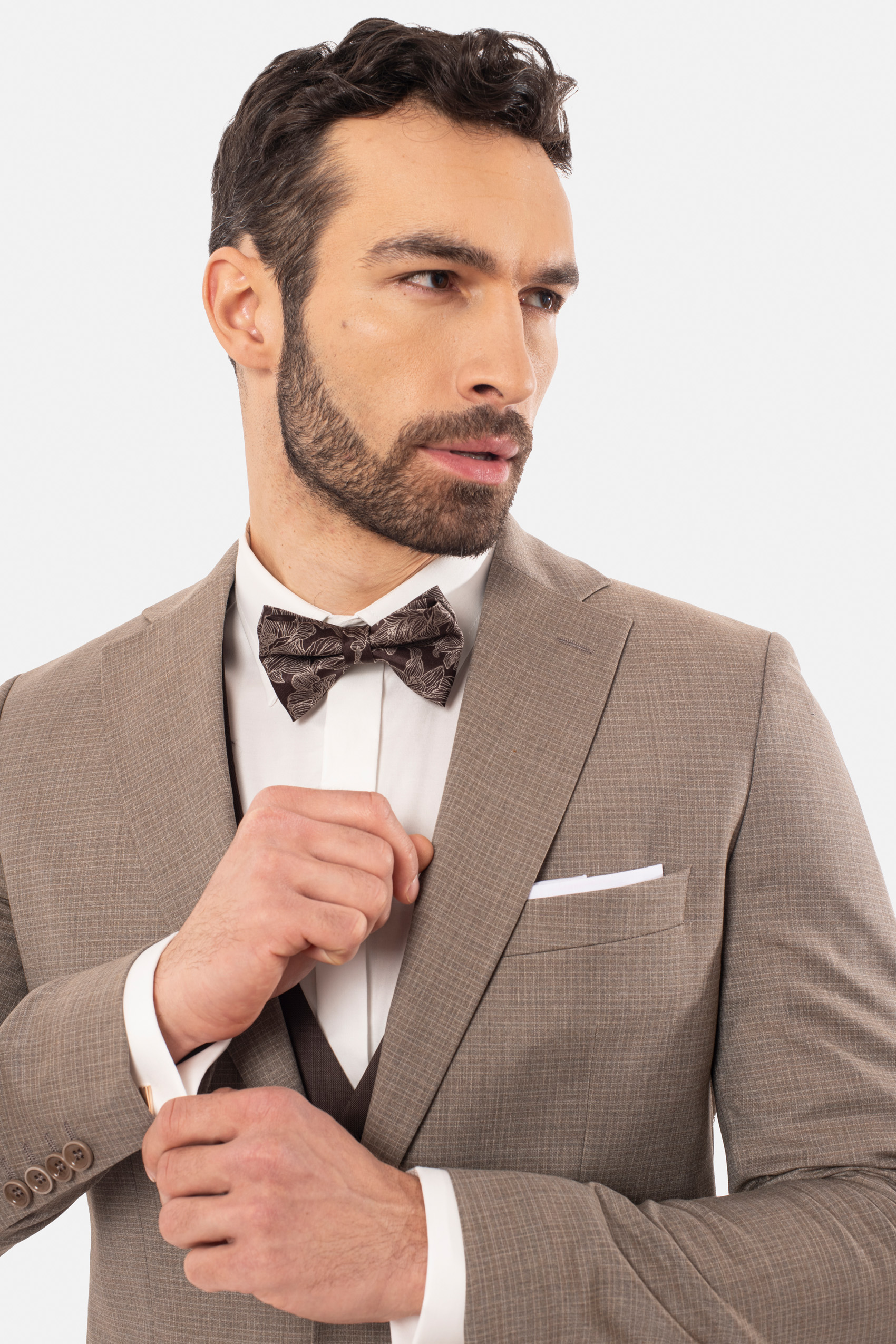 Mężczyzna ubrany w beżową marynarkę, białą koszulę i muchę w kolorze brązowym ze wzorami