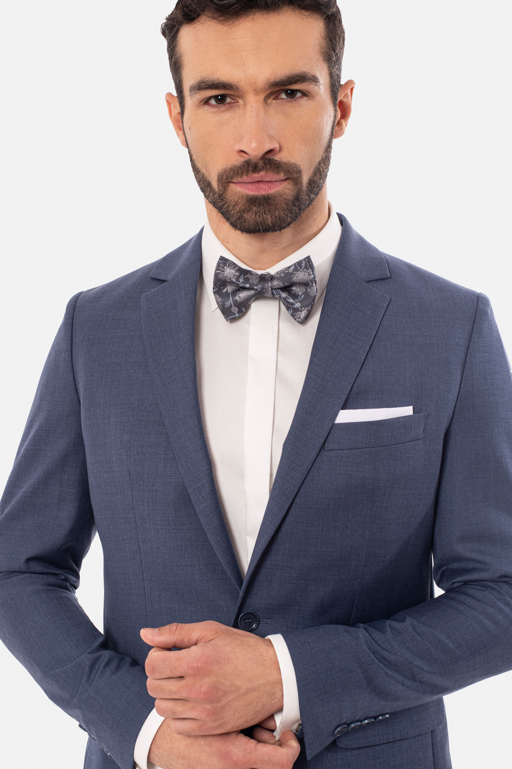 Mężczyzna ubrany w białą koszulę, szarą muszkę w kwiatki i niebieską marynarkę